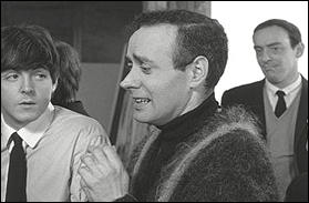 Character actor, John Junkin, looks on in the background at Victor Spinetti talks with Paul McCartney in a scene from The Beatles first feature film, A Hard Day's Night.