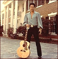 Kurt Russell as Elvis Presley. He is standing in front of Graceland.